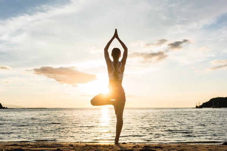 Silhouette einer Frau, die die Baum-Yoga-Pose an einem Strand übt