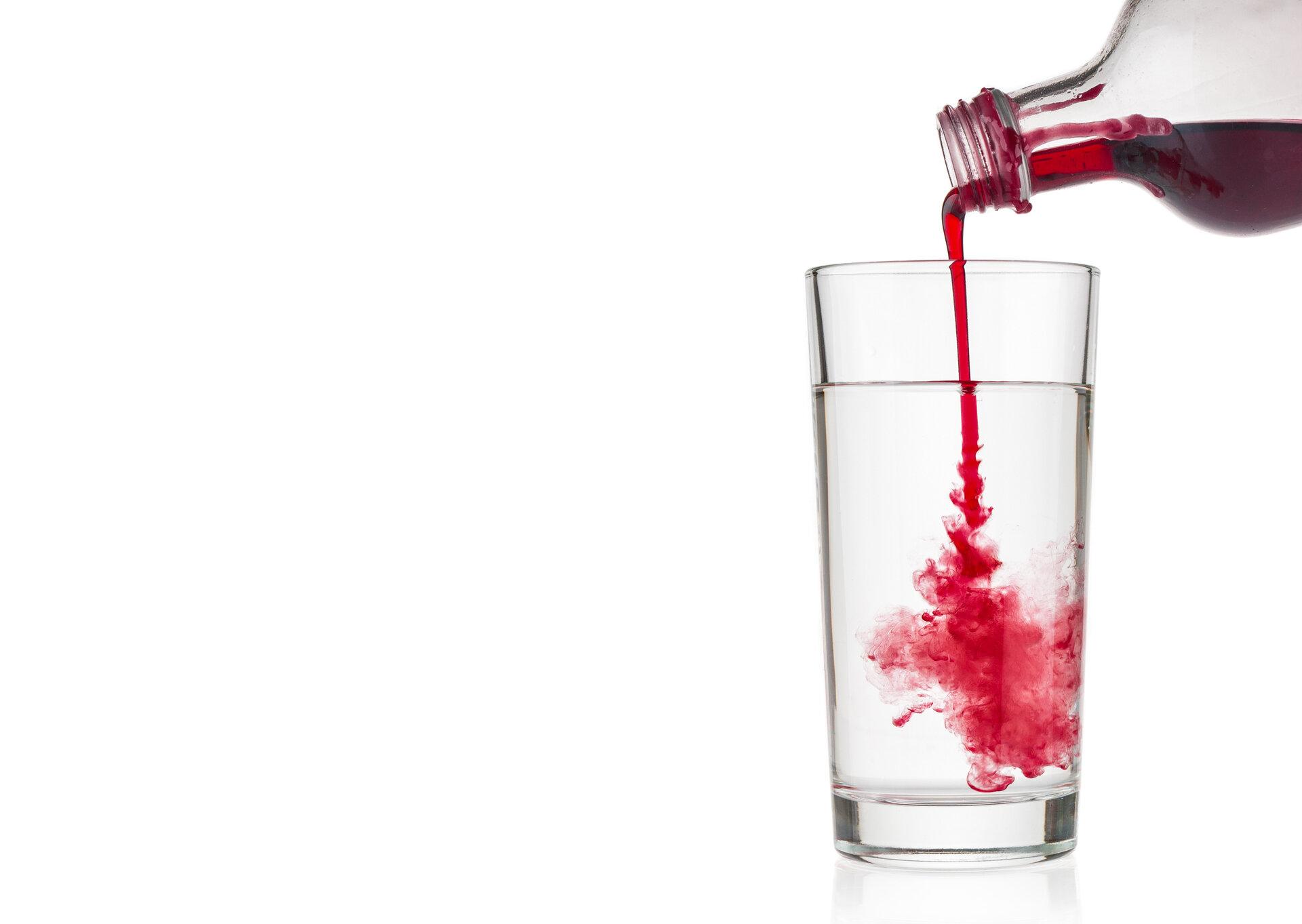 Cranberry-Sirup gießt in Wasserglas auf weißem Hintergrund