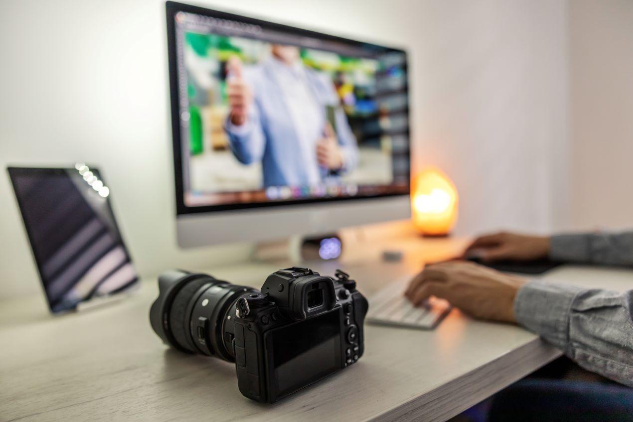 Eine Kamera auf einem Schreibtisch vor einem Monitor mit Bildbearbeitungssoftware – perfekte Darstellung der Nachbearbeitung nach dem Dias digitalisieren.